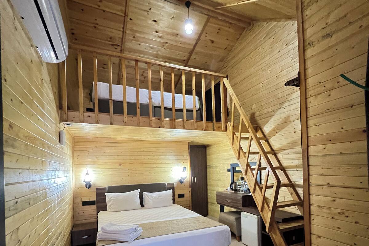 A wooden cabin room with a bed, a desk, and a staircase.