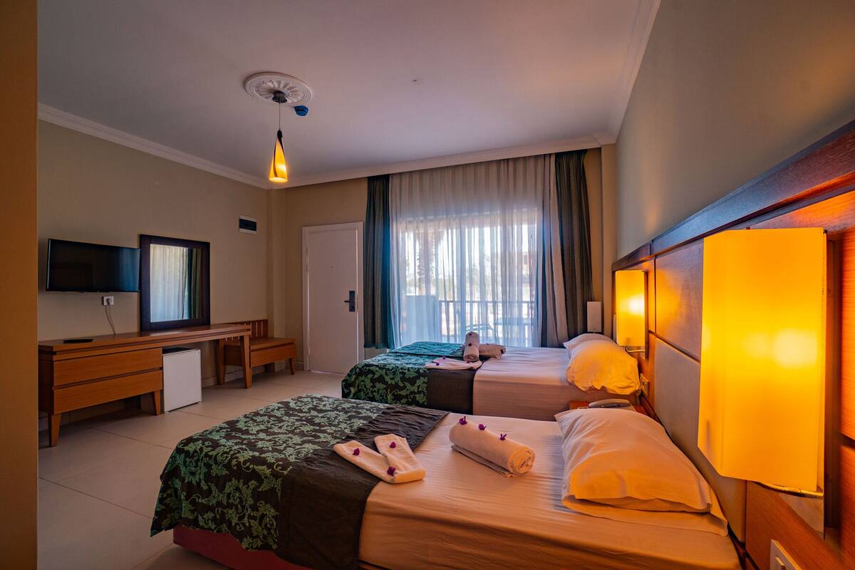 A hotel room with two beds, a desk, a television, and a window with curtains.