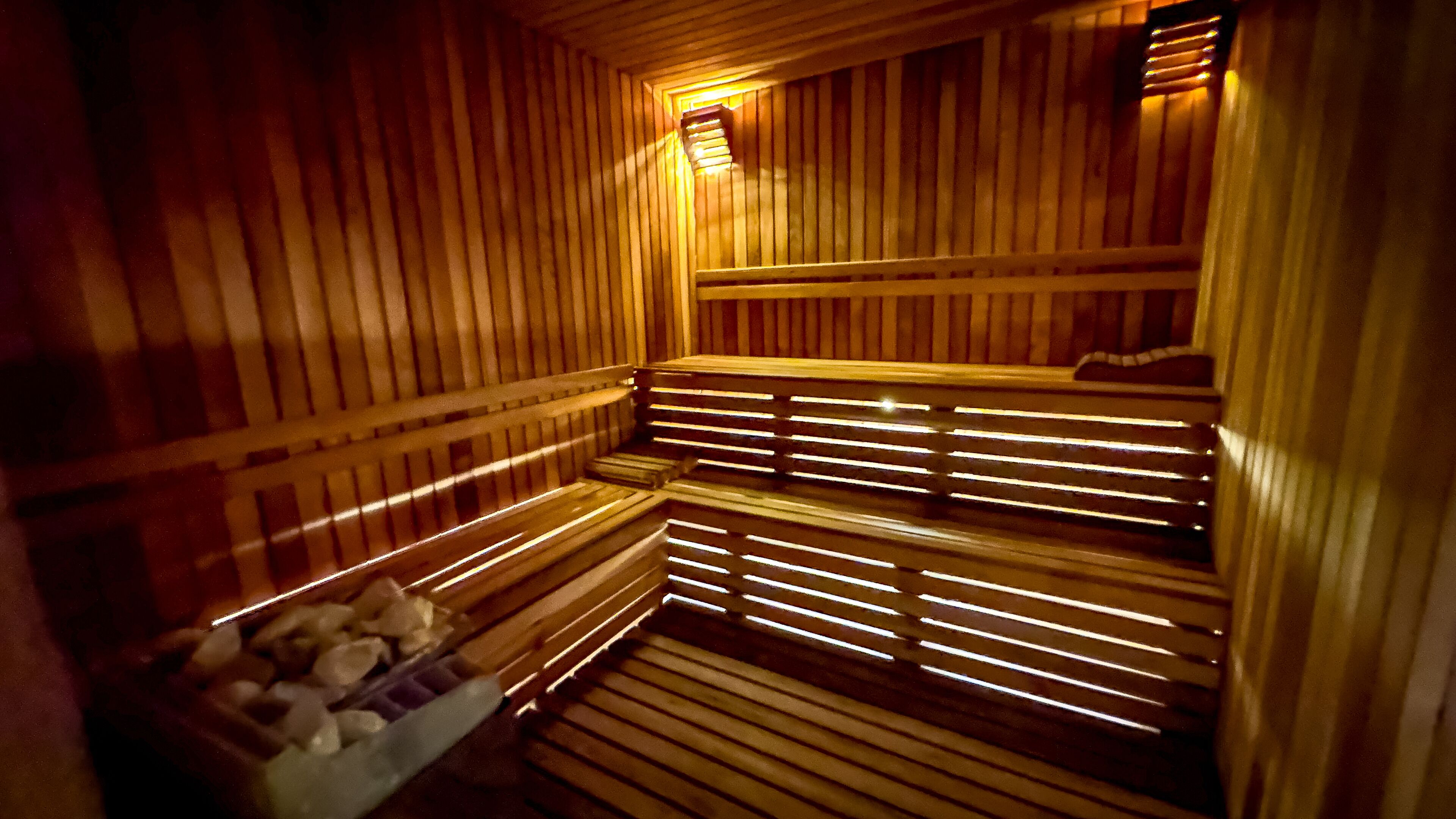 En sauna med træbænke og en bænk med en beholder med sten.