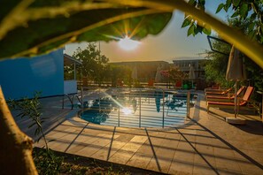 Une piscine où les rayons du soleil filtrent à travers le feuillage, entourée de chaises longues et de parasols.