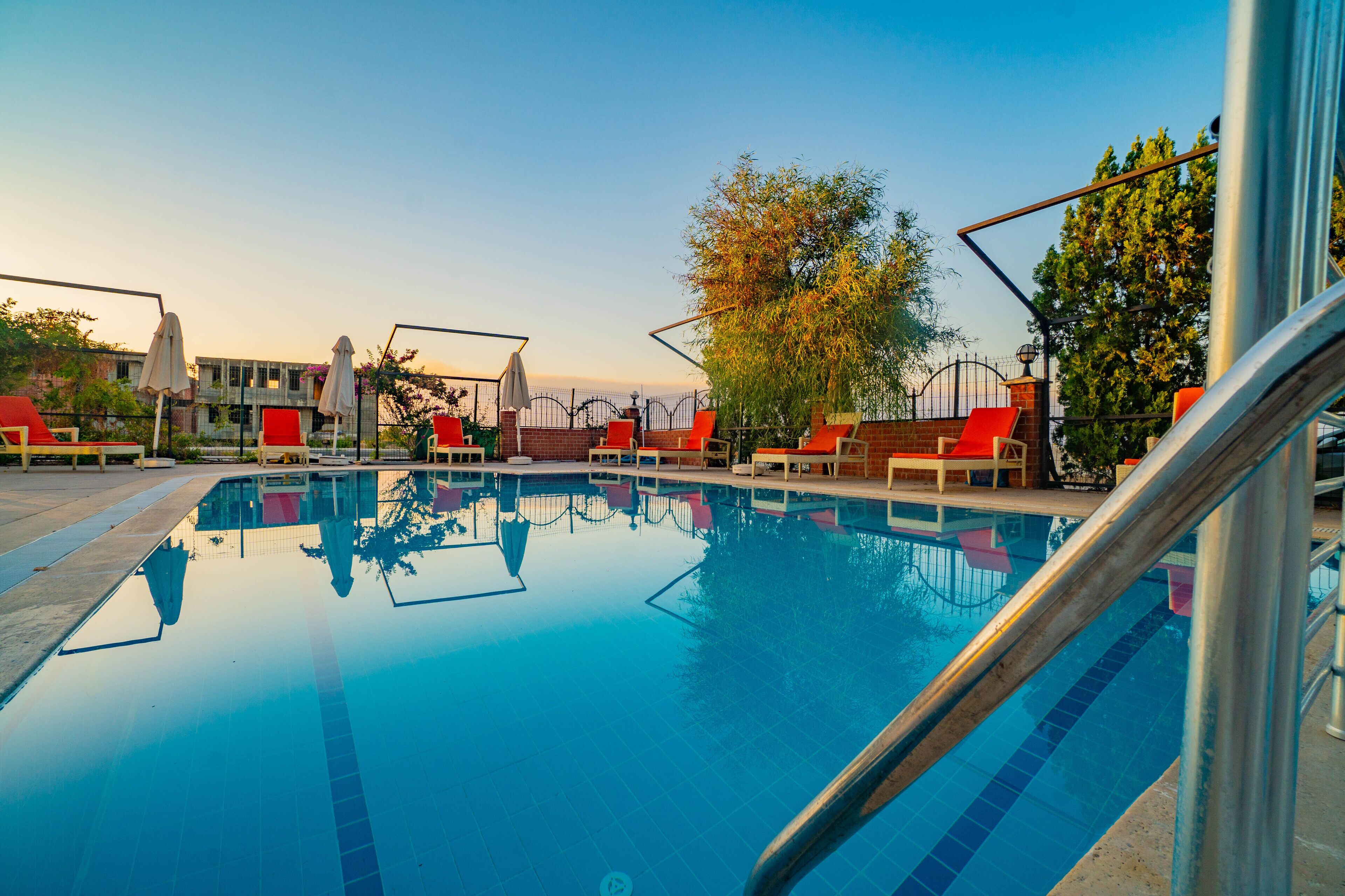 A swimming pool with red lounge chairs and a metal railing.