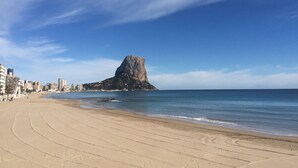 Une plage avec une formation rocheuse imposante à l’horizon, un rivage sablonneux et des bâtiments le long de la côte.