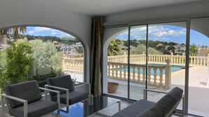 Un balcon avec une table en verre, deux canapés gris et une vue sur une piscine et des maisons.