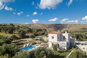 Una villa de piedra con piscina, rodeada de olivos y un paisaje montañoso.