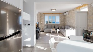 Una cocina moderna con un refrigerador de acero inoxidable, una zona de comedor con una mesa y sillas blancas, una pared de piedra y un amplio ventanal con vistas.