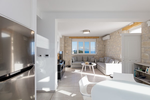 Una cocina moderna con un refrigerador de acero inoxidable, una zona de comedor con una mesa y sillas blancas, una pared de piedra y un amplio ventanal con vistas.