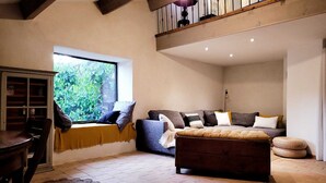 A cozy living room with a sofa, ottoman, and a window with a view of greenery. - Au Mûrier Blanc (Collias)
