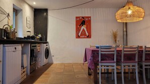 A compact kitchen with a washing machine, a dining area with a table and chairs, and a decorative poster on the wall. - Au Mûrier Blanc (Collias)