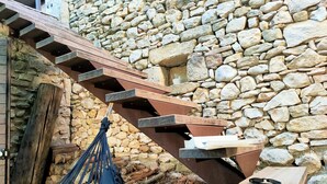 A wooden staircase with stone walls, a hammock, and a table with sunglasses. - Au Mûrier Blanc (Collias)