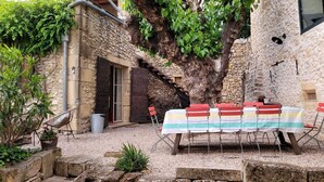 A rustic outdoor seating area with a stone wall, a wooden staircase, and a large tree. - Au Mûrier Blanc (Collias)