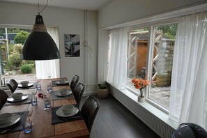 En spiseplads med et træbord dækket til seks personer, sorte stole og en hængende lampe.