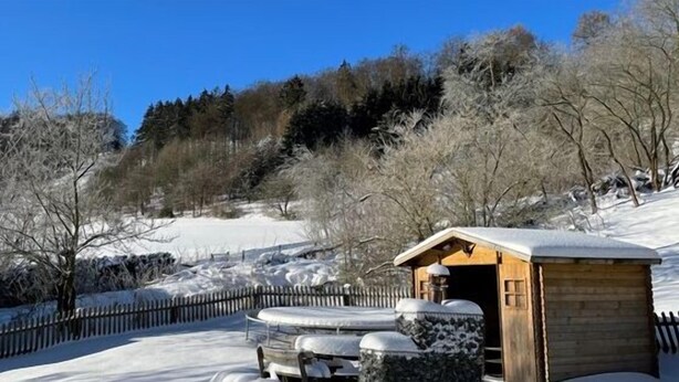 Una cabaña de madera con techo nevado, rodeada por un paisaje cubierto de nieve y una valla de madera.