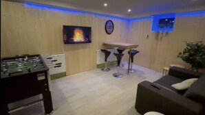 Una habitación con mesa de fútbol, dos taburetes de bar, un sofá y televisor montado en la pared.