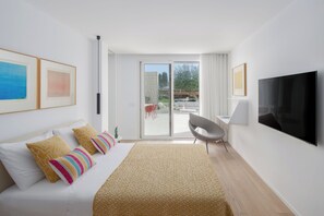 A modern hotel room with a bed, a desk, a TV, and a sliding glass door to the outside.