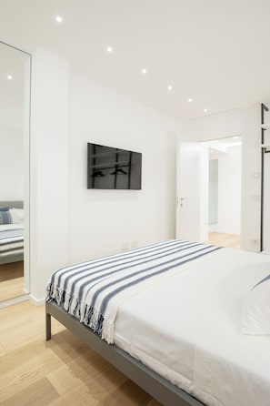 A modern bedroom with a bed, a wall-mounted TV, and a door leading to another room.