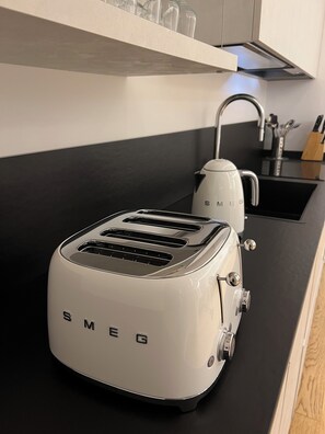 A kitchen with a white Smeg toaster, a kettle, and a black countertop.