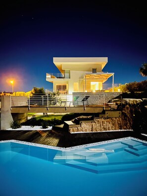 A modern house with a swimming pool, a balcony, and a view of the night sky.