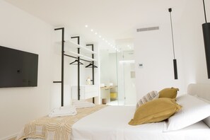 Une chambre d’hôtel moderne équipée d’un lit, d’une télévision, d’une armoire et d’une salle de bain visible à travers une porte en verre.