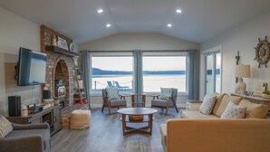 A spacious living room with a fireplace, a television, and a view of the water. - Sunrise@Potlatch-Waterfront Luxury Home Hood Canal (Shelton)