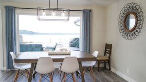 A dining area with a large table, four chairs, a wooden floor, a view of the water, and a decorative mirror on the wall. - Sunrise@Potlatch-Waterfront Luxury Home Hood Canal (Shelton)