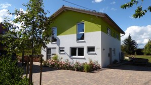 A two-story house with a green and white facade, multiple windows, and a brick driveway. - Room with private bathroom in detached house (Königsfeld im Schwarzwald)