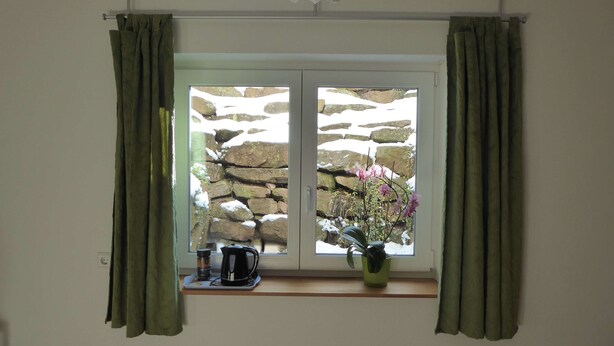 A window with green curtains, a stone wall outside, and a potted plant on the windowsill. - Room with private bathroom in detached house (Königsfeld im Schwarzwald)