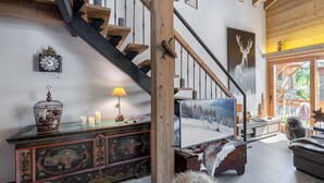 Eine Treppe mit Holzgeländern und einem schwarzen Handlauf, ein alter Schrank mit dekorativen Malereien, ein Fernseher auf einem Holzboden und ein Hund, der auf dem Boden sitzt.