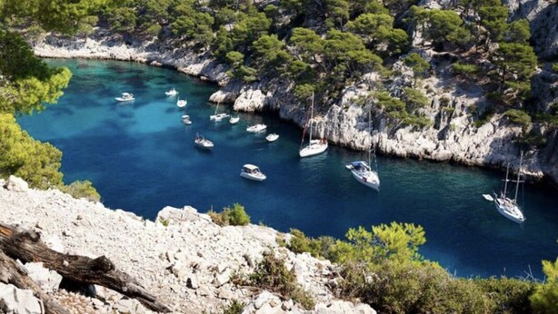 A coastal landscape with rocky terrain, dense green trees, and a clear blue sea with boats anchored. - Appartement Villa Cassis (Cassis)