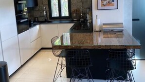 A modern kitchen with a central island, black bar stools, and pendant lighting. - Appartement Villa Cassis (Cassis)