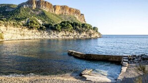 A coastal scene with a rocky cliff, clear water, and a small dock. - Appartement Villa Cassis (Cassis)