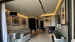A modern living room with a sofa, coffee table, and decorative items. There is a dining area with chairs and a table. - Appartement Villa Cassis (Cassis)