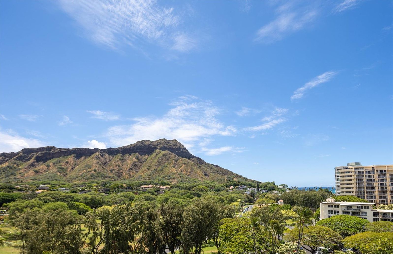 A mountainous landscape with a clear sky, surrounded by greenery and residential buildings.
