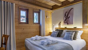 Une chambre aux murs lambrissés, avec un grand lit, deux fenêtres, une table de chevet et une chaise.