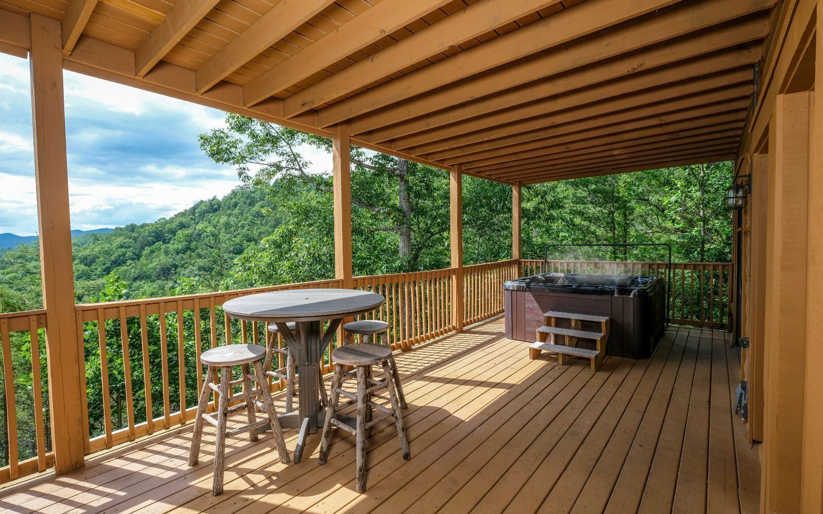 Une terrasse en bois avec un jacuzzi, une table et quatre tabourets.