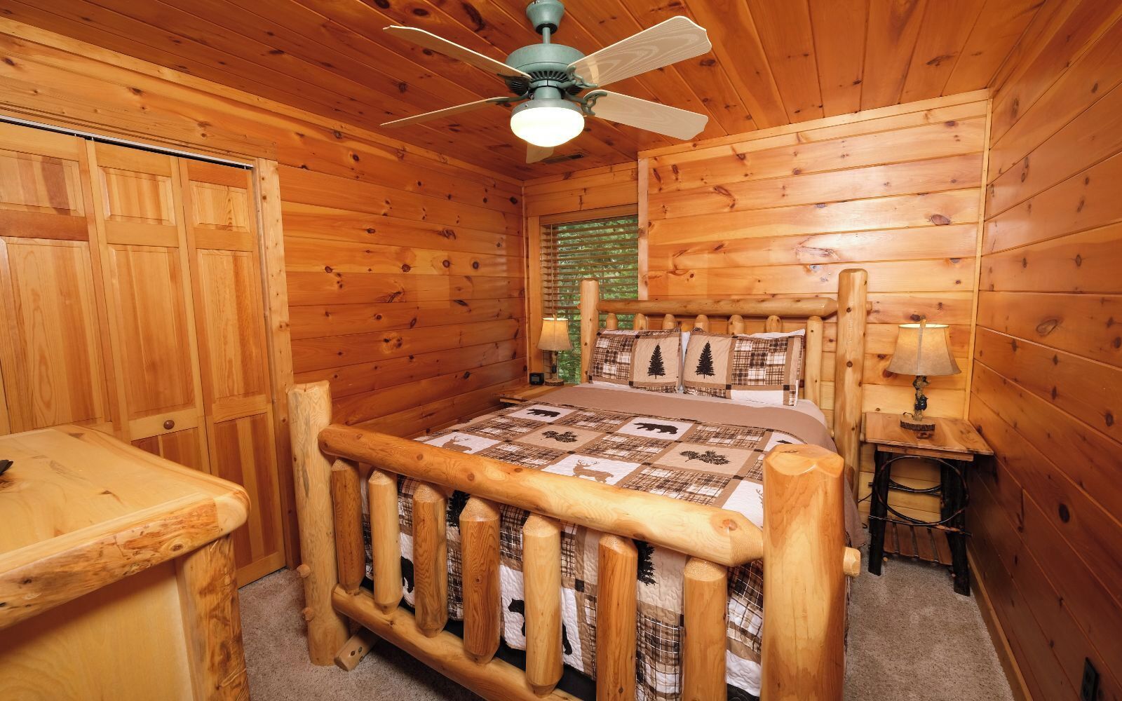 A wooden cabin bedroom with a bed, a nightstand, a lamp, and a ceiling fan.