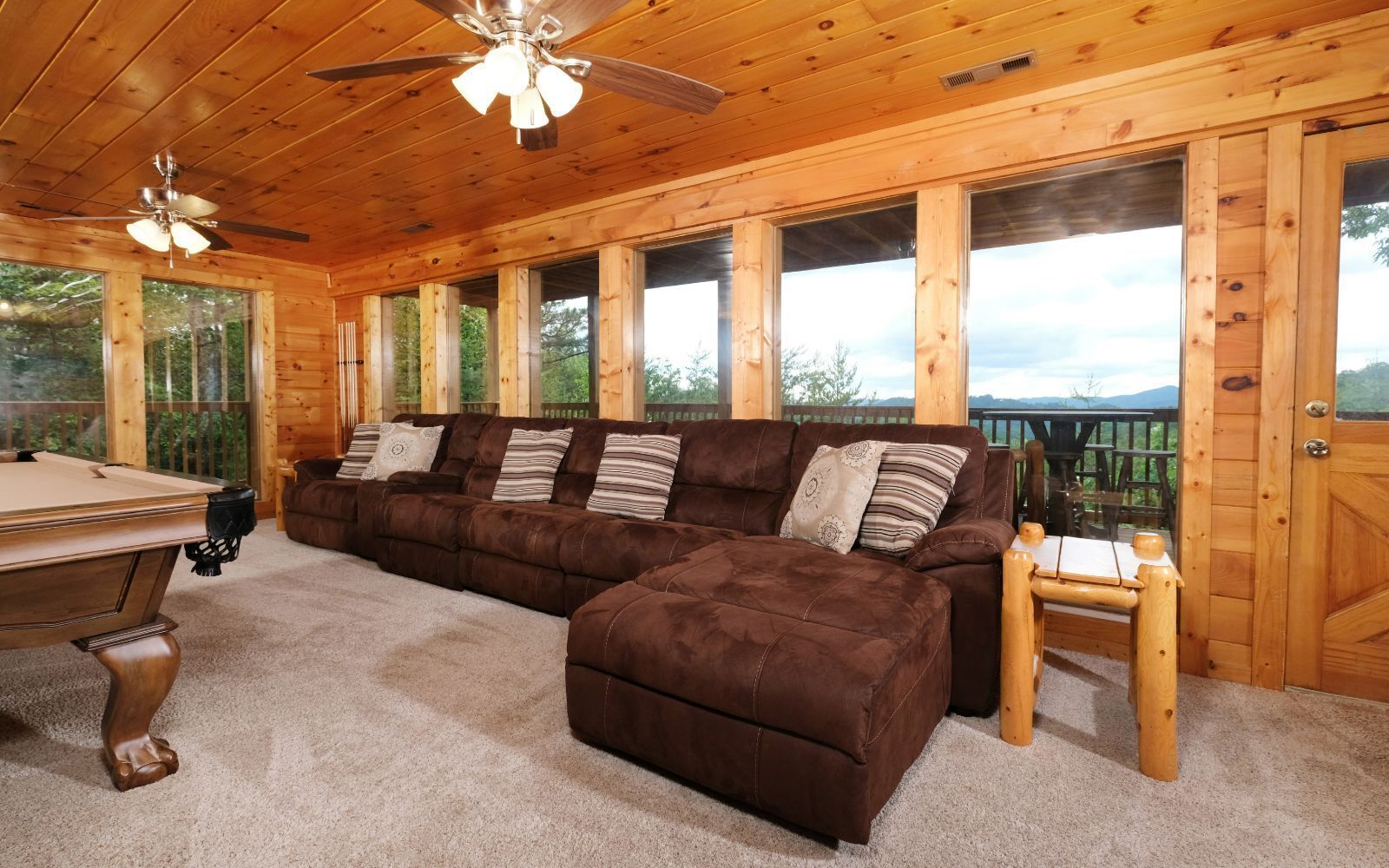 Une cabane en bois avec un grand canapé marron, une table de billard et un ventilateur de plafond.