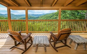 A wooden deck with two Adirondack chairs and a small table, overlooking a forested mountain range. - Cali's Place - Gorgeous Mountain Views, Pet Friendly, Hot Tub + Pool Table (Sevierville)