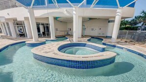 A pool area with a circular hot tub and a separate pool, surrounded by a covered deck with white columns and a blue-tiled floor. - New Top Floor Direct Oceanfront with Amazing View! (Myrtle Beach)