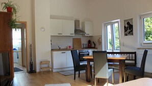Una cucina moderna con mobili bianchi, un tavolo da pranzo in legno e sedie nere. Una finestra offre luce naturale e vista su piante.