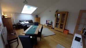 A living room with a sofa, TV, dining table, and a skylight.