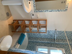 Bathroom features a white toilet, sink, and shower area with mosaic tiles, along with a storage shelf.