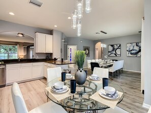 A modern kitchen with white cabinets, a dining area with a glass table, and abstract wall art.