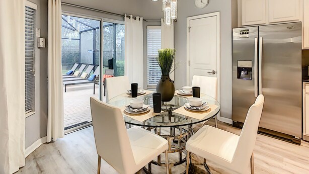 A modern kitchen with a stainless steel refrigerator, a dining table with chairs, and a glass-top table with a vase. - Luxury 6BR | Game Room, Outdoor Theater & Pool/Spa (Kissimmee)