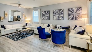 A modern living room with a white sofa, blue chairs, a coffee table, and abstract wall art. - Luxury 6BR | Game Room, Outdoor Theater & Pool/Spa (Kissimmee)
