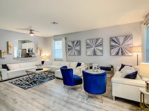 A modern living room with a white sofa, blue chairs, a coffee table, and abstract wall art.
