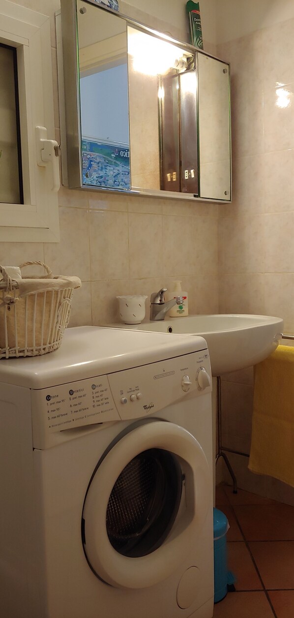 Un área de lavandería compacta con lavadora, lavabo y espejo superior.