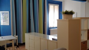 Een kamer met een wit bureau, een stoel, een kast met manden, en een raam met gordijnen.