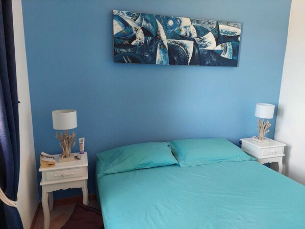 Camera da letto con un letto, due comodini, un tavolino e un quadro appeso al muro, oltre a una tenda.