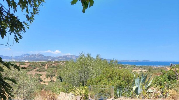 A wooden table with a glass on it, set on a patio overlooking a scenic landscape with mountains and a body of water in the distance. - Sea view, Pleasant house in the heart of olive groves in the countryside (Murta Maria)