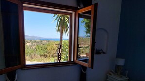 A bedroom with a large window offering a view of a palm tree and distant landscape. - Sea view, Pleasant house in the heart of olive groves in the countryside (Murta Maria)